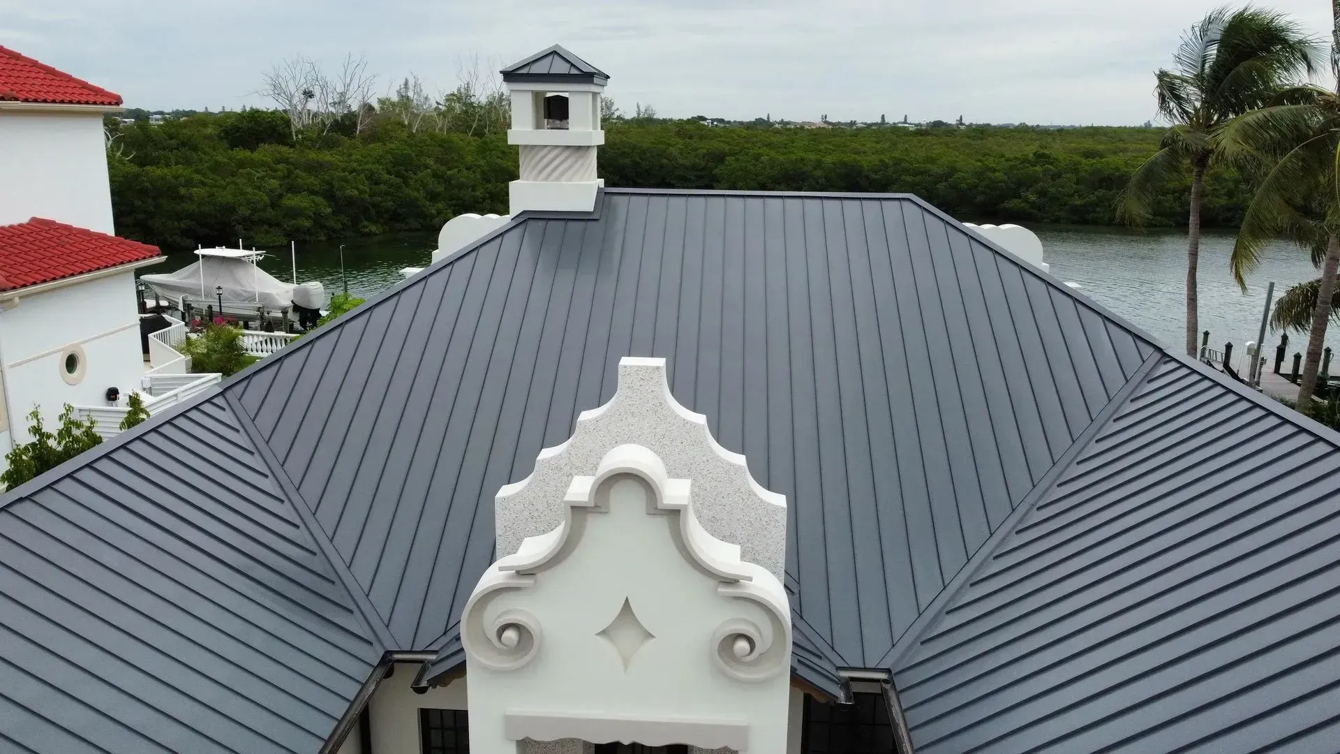 Gray metal roof with white architectural details; background of trees and water.