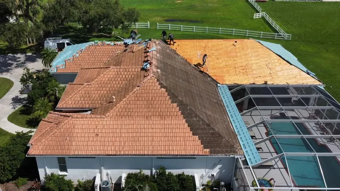 House with a section of roof under construction, surrounded by a pool, and green lawn.