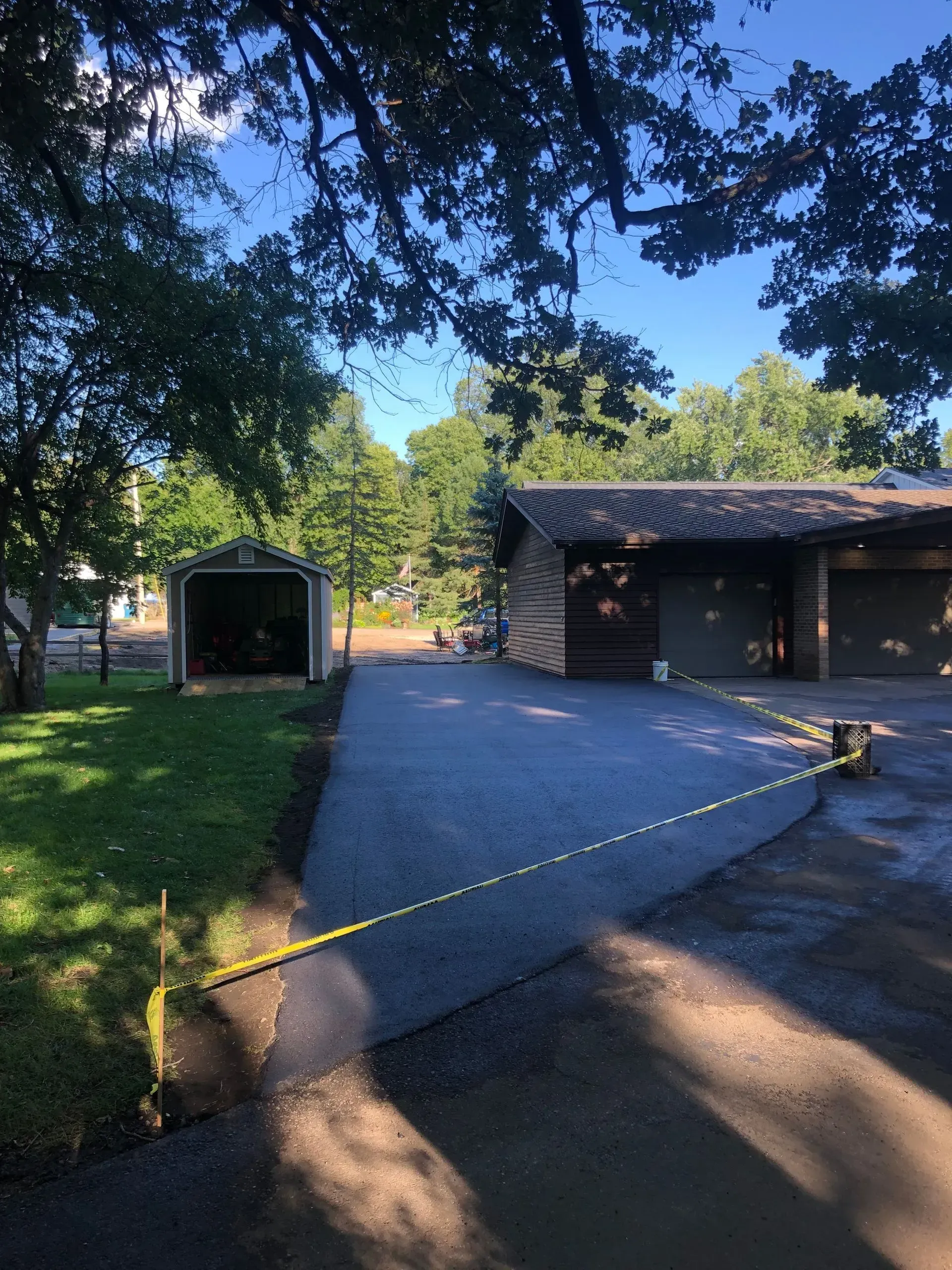 Driveway with caution tape in front of a house, a small shed, and trees in evening light