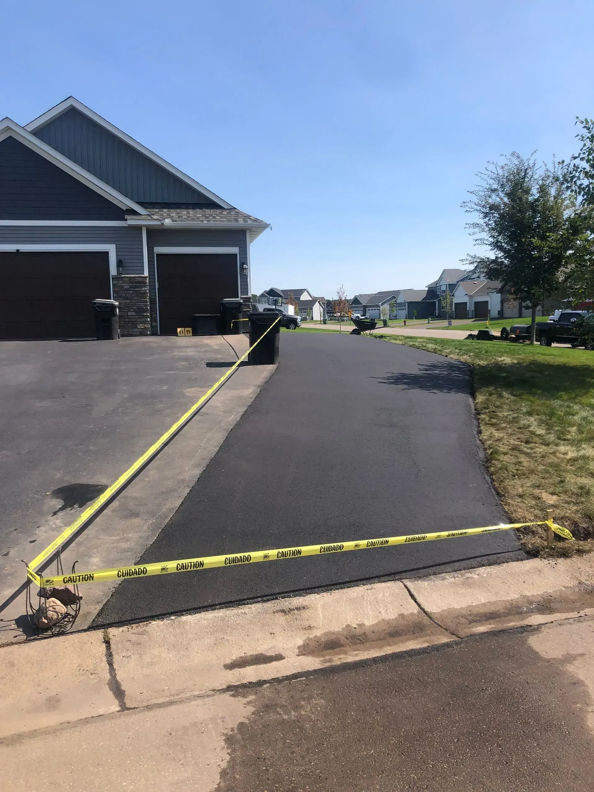 Driveway entrance blocked off with yellow caution tape beside a house on a sunny street.
