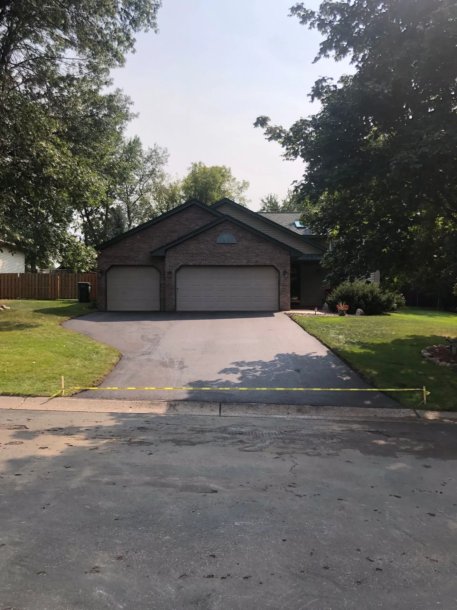 Driveway leading to a two-car garage with brick exterior, framed by trees and a lawn.