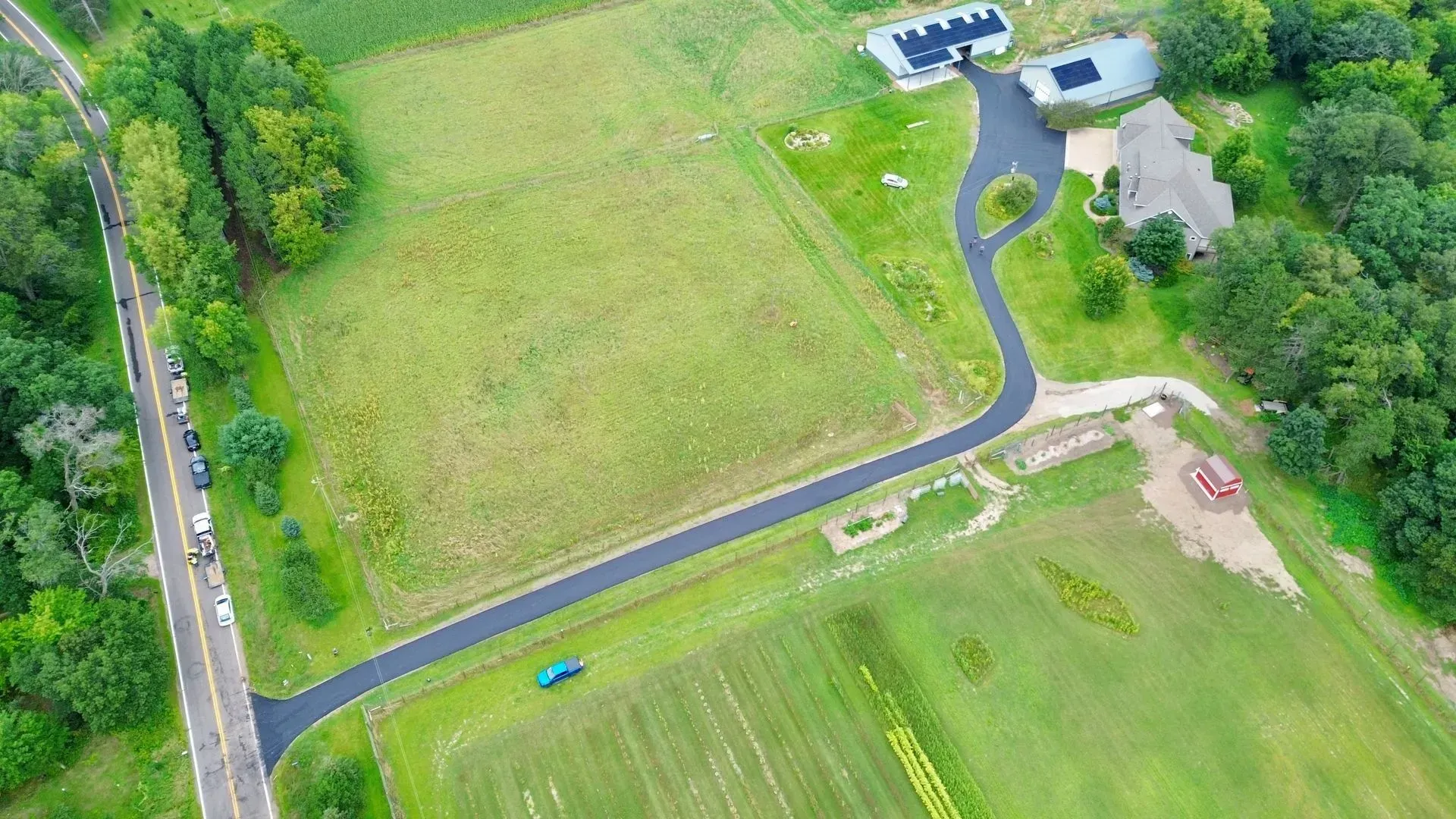 Aerial view of a rural property with a house, driveway, green fields, and nearby road