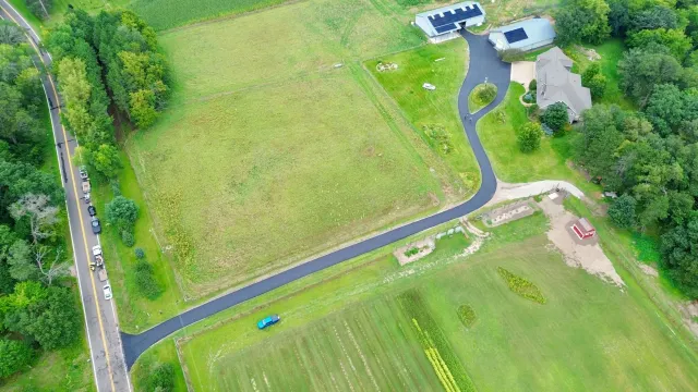 Aerial view of a rural property with a house, driveway, green fields, and nearby road