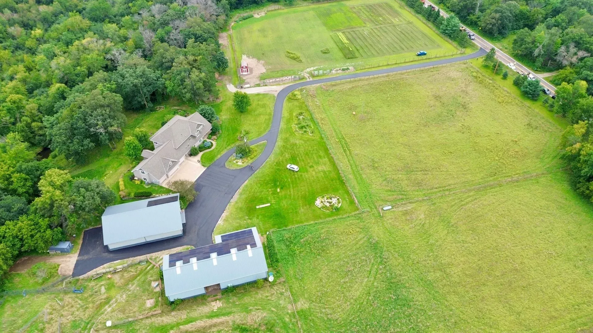 Aerial view of a rural property with several buildings, a driveway, and large green fields.