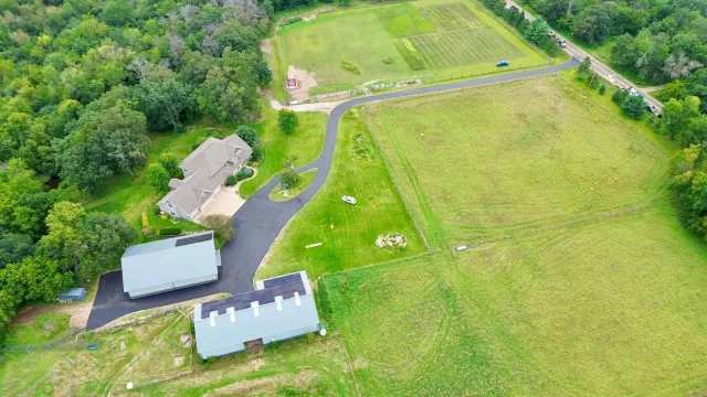 Aerial view of a rural property with several buildings, a driveway, and large green fields.
