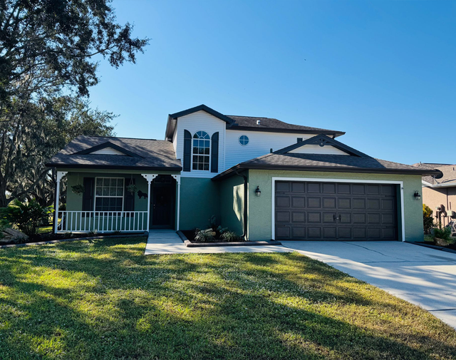 Suburban house with teal exterior, front porch, two-car garage, and sunlit lawn