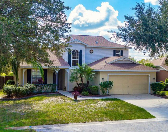 Suburban two-story house with garage, front lawn, and palm trees under a sunny sky