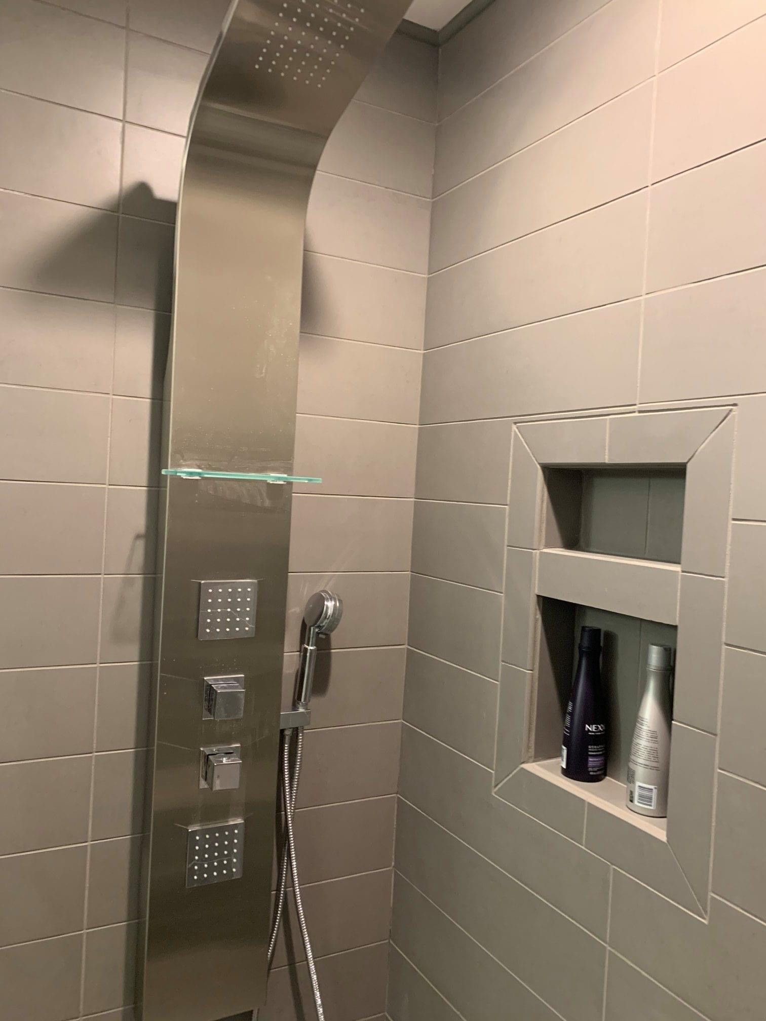 A shower with a stainless steel shower head and a shelf with bottles on it