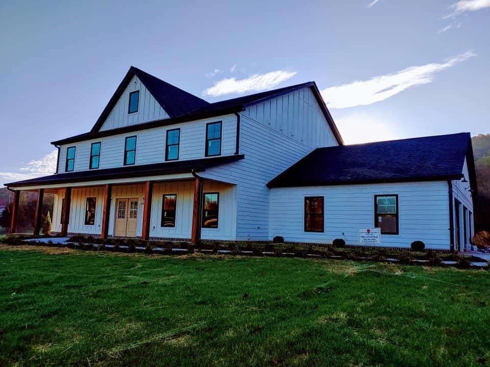 A large white house with a black roof is sitting on top of a lush green field