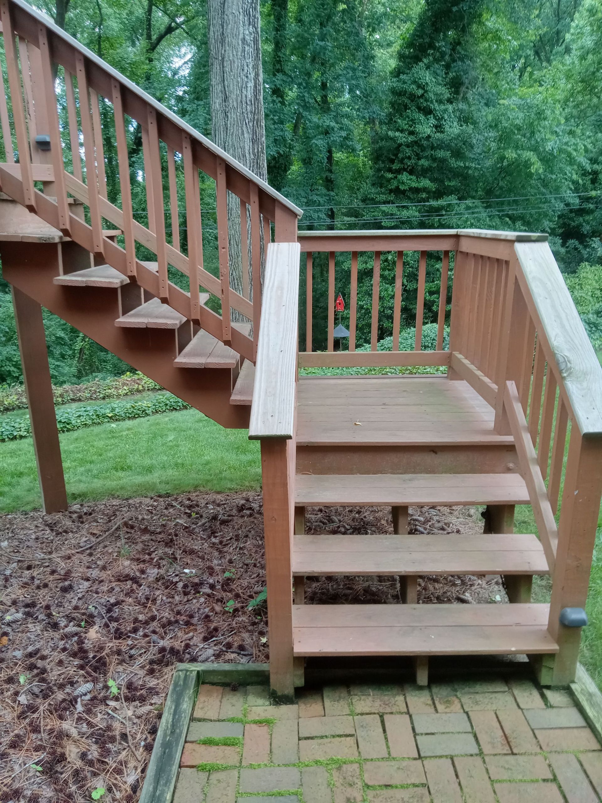 Wooden outdoor staircase with railings, leading up to a deck and down to a brick patio.