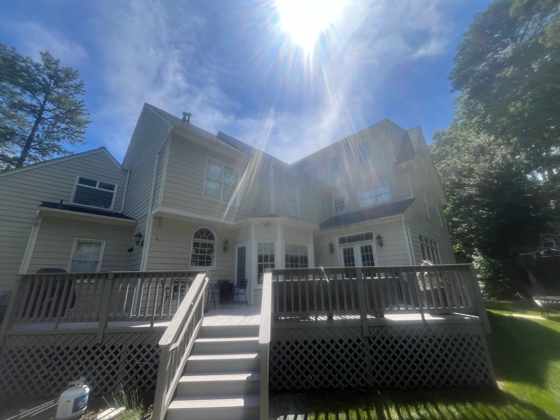 Two-story house with a wooden deck and staircase, under a bright, sunny sky.