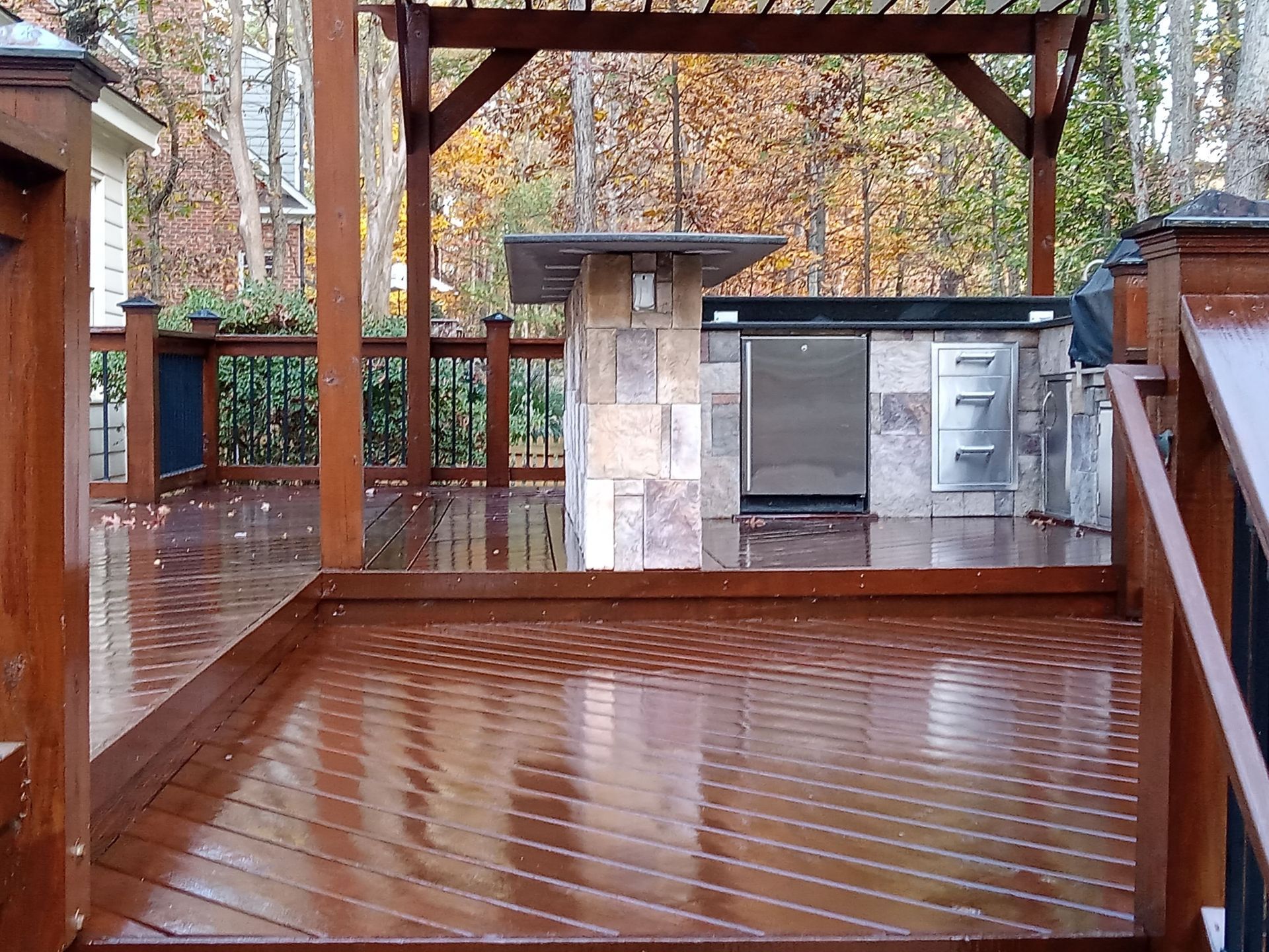 Wooden deck with outdoor kitchen under a pergola. The deck is wet and shiny.