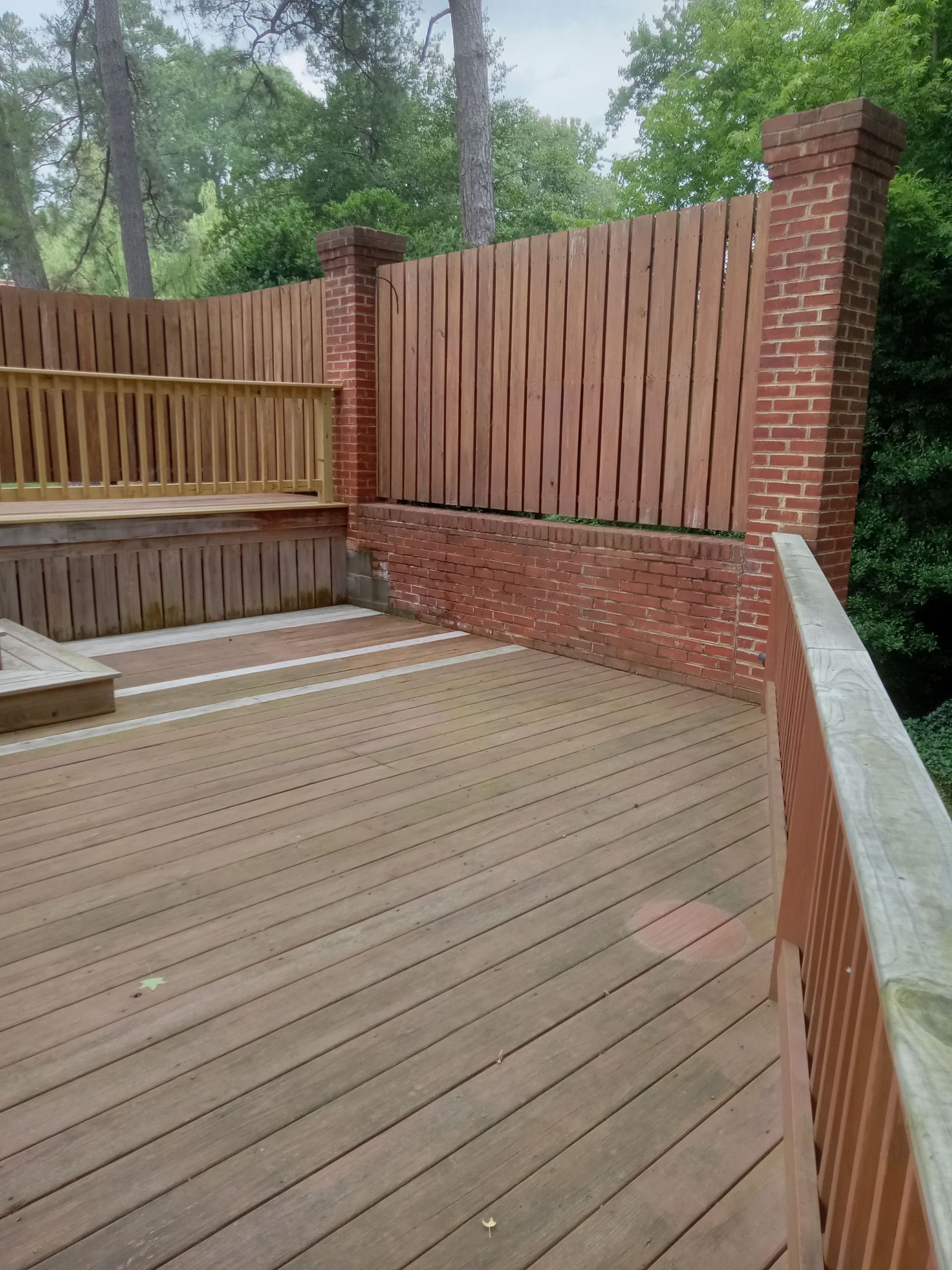 Wooden deck with a brick and wood privacy fence in a wooded setting.