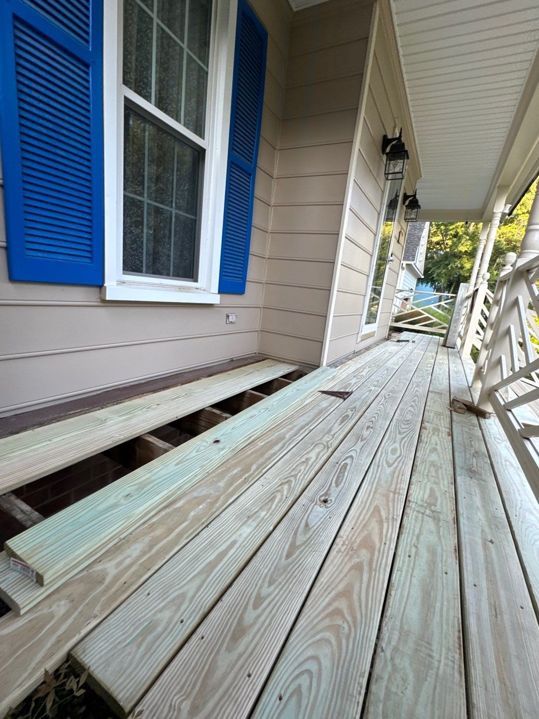 Porch with missing deck boards, blue shutters, and siding.