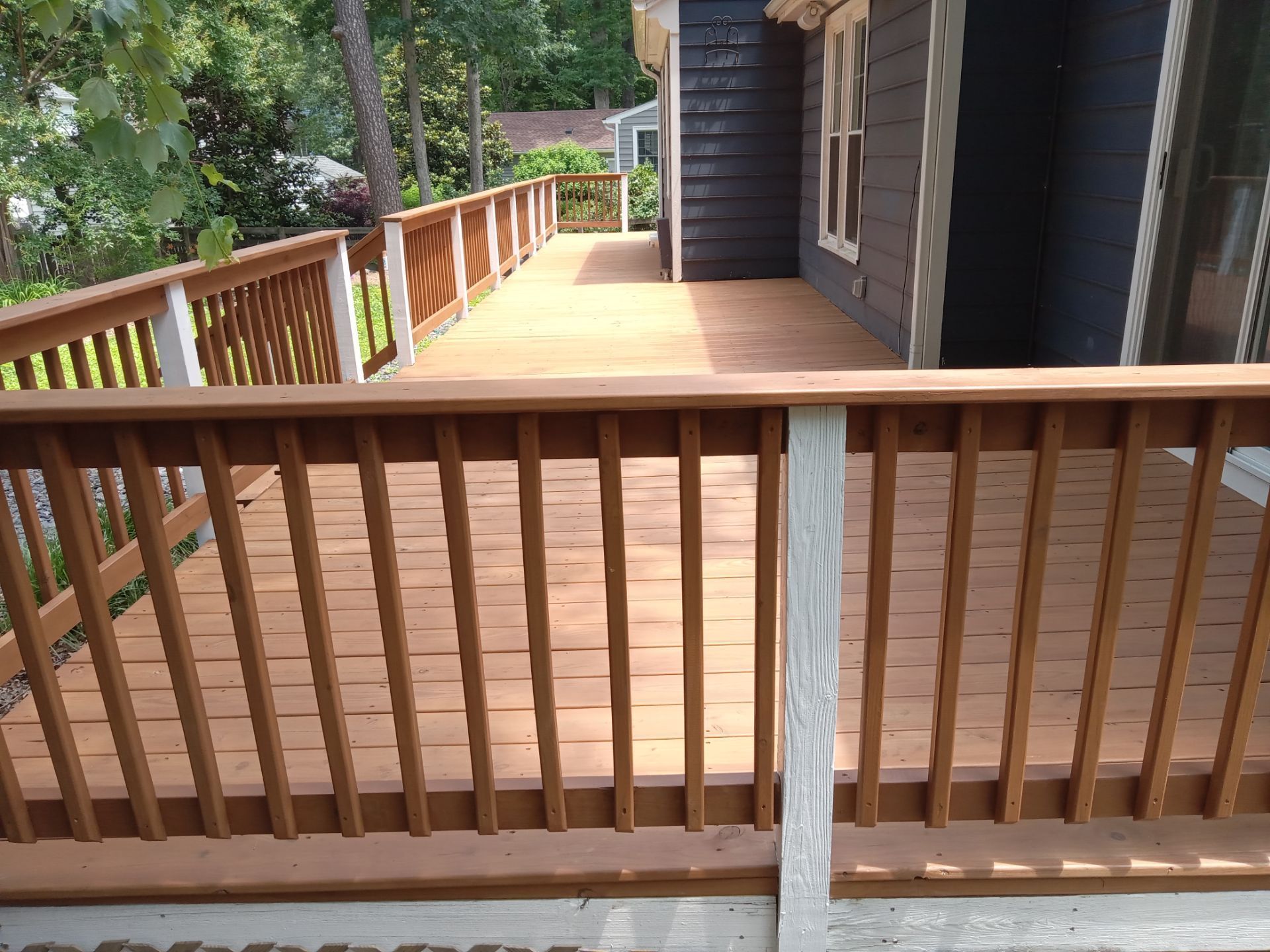Wooden deck with brown planks and railing next to a dark-colored house, surrounded by trees.