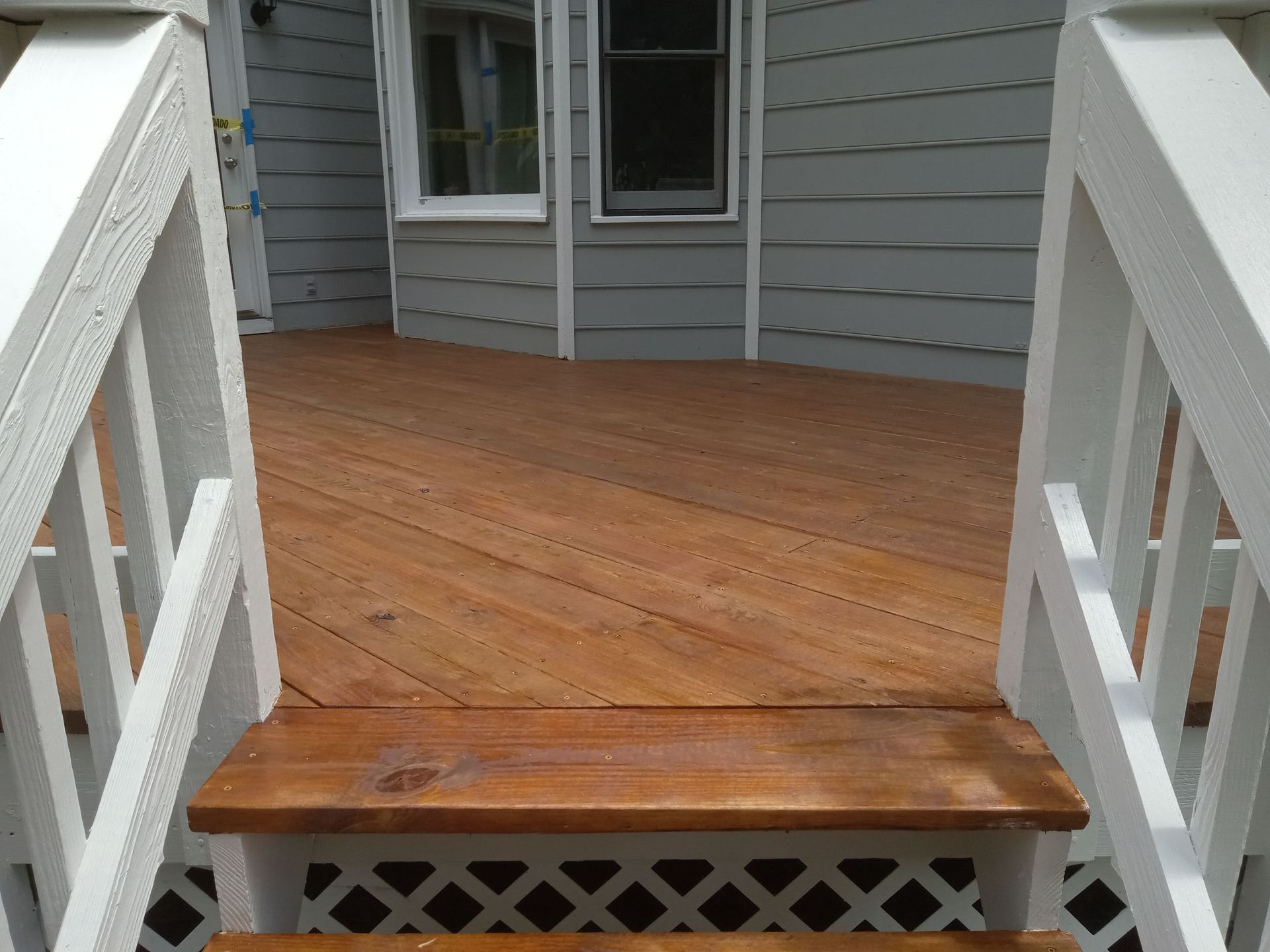 Wooden deck with white railings, leading to a house with gray siding.