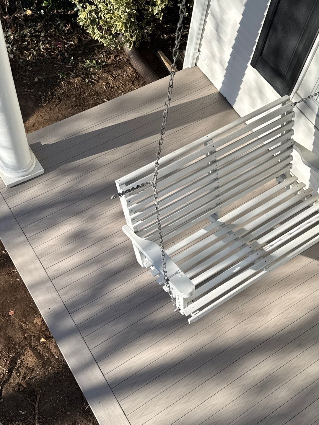 White porch swing on a composite deck, near a white column and house.