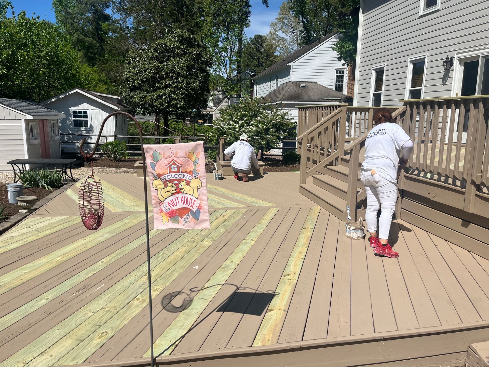 Two people painting a wooden deck with a geometric design. The deck is in a backyard.