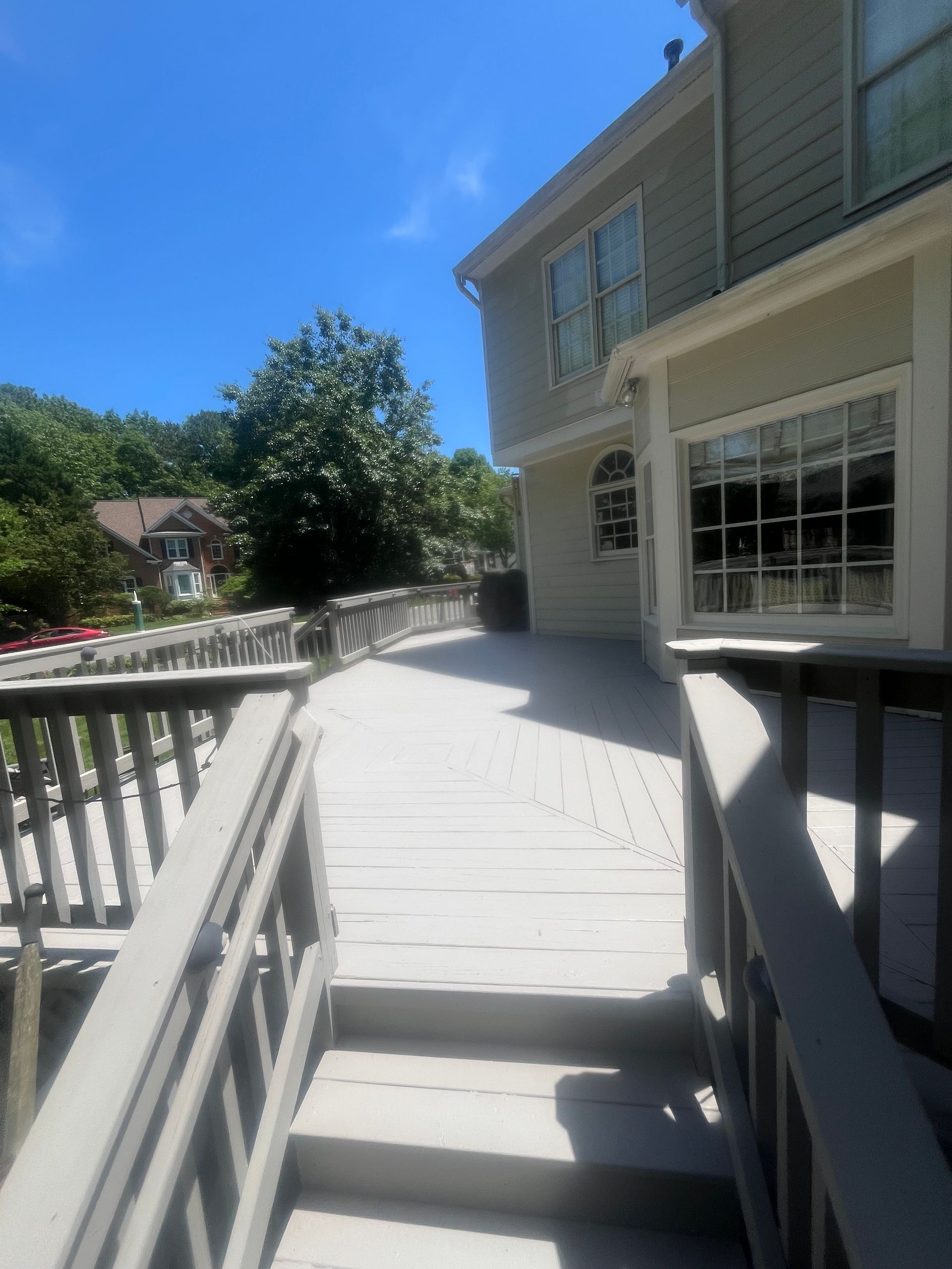 Grey wooden deck attached to a light-colored house on a sunny day.