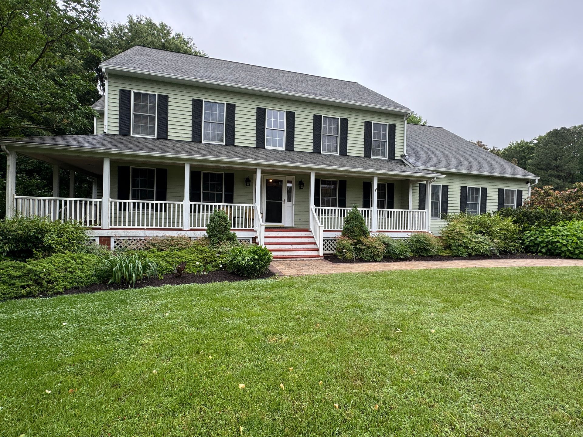 Two-story house with green siding, white porch, black shutters, and a green lawn.