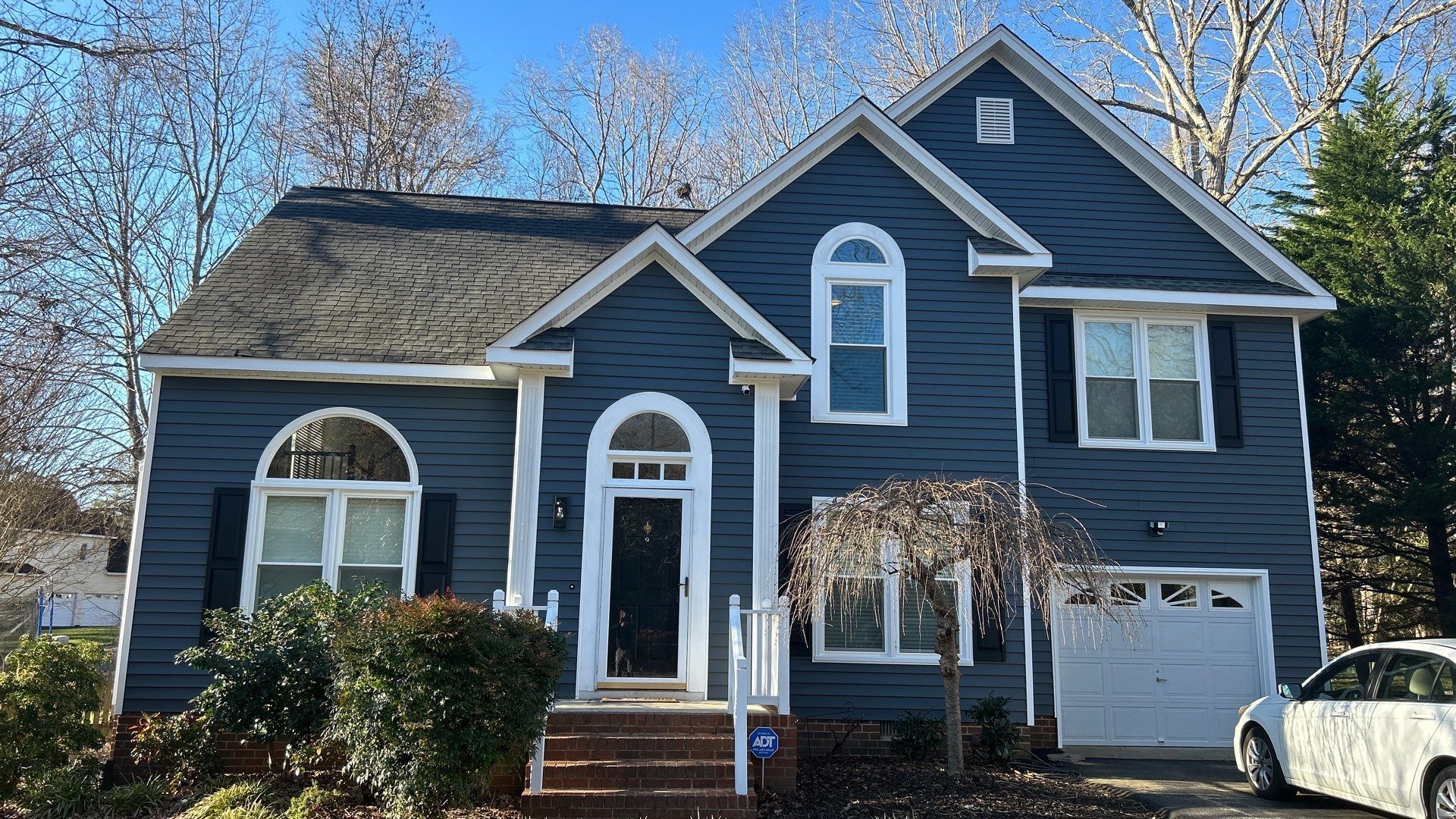 Blue two-story house with white trim, dark roof, and a single-car garage. A car is parked on the side.