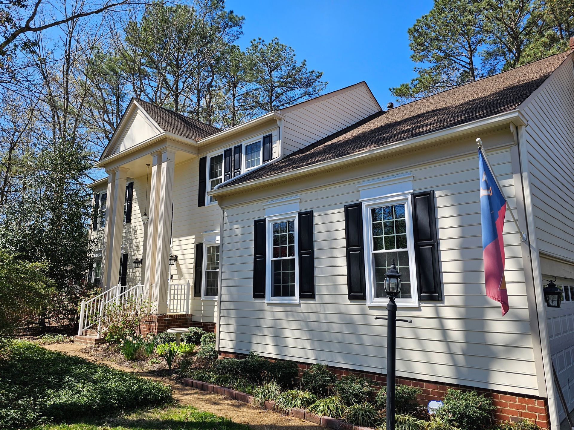 Two-story beige house with black shutters, white columns, and a flag.