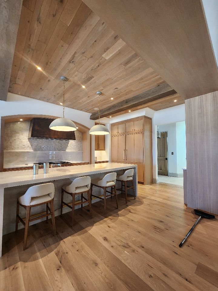 Kitchen with light wood ceiling, island with stools, and light wood flooring.