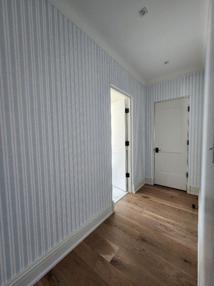 Narrow hallway with blue and white striped wallpaper, wood floor, and white doors.