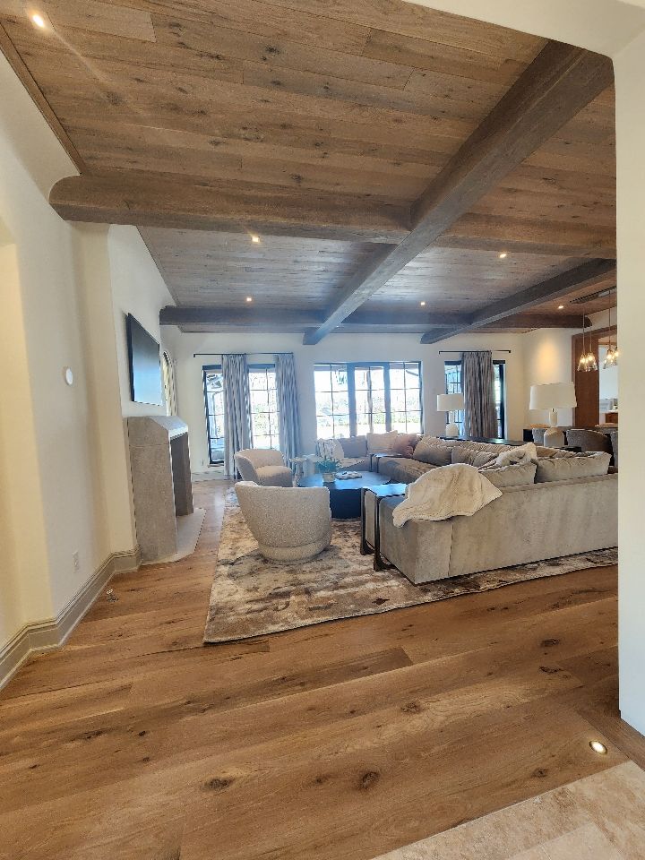 Living room with wood floors and ceiling beams, light-colored walls, furniture, and a stone fireplace.