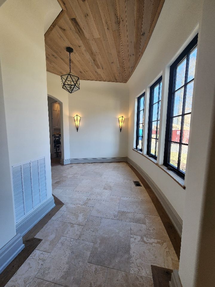 Hallway with wood ceiling, sconces, windows, and stone floor.