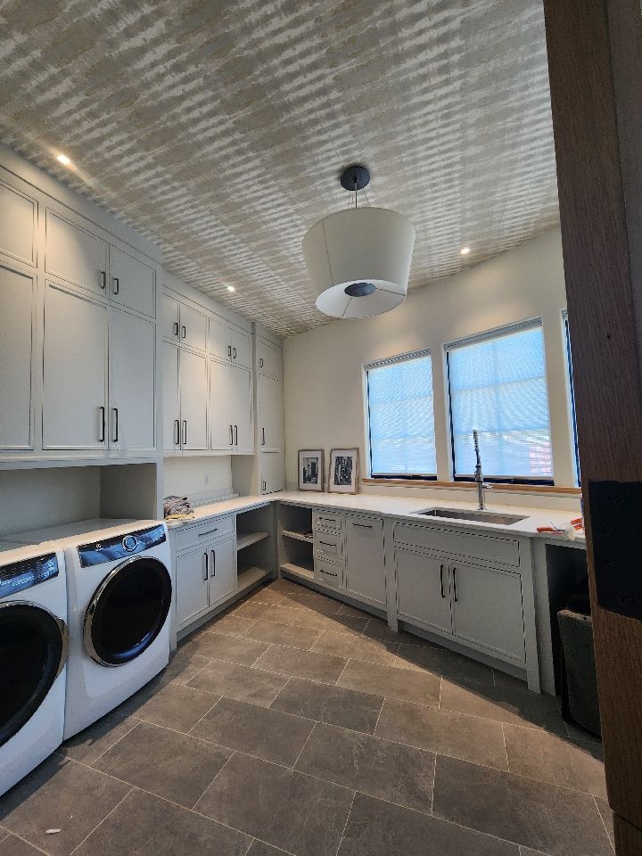 Laundry room with gray cabinets, washer/dryer, sink, windows with blinds, and decorative ceiling.