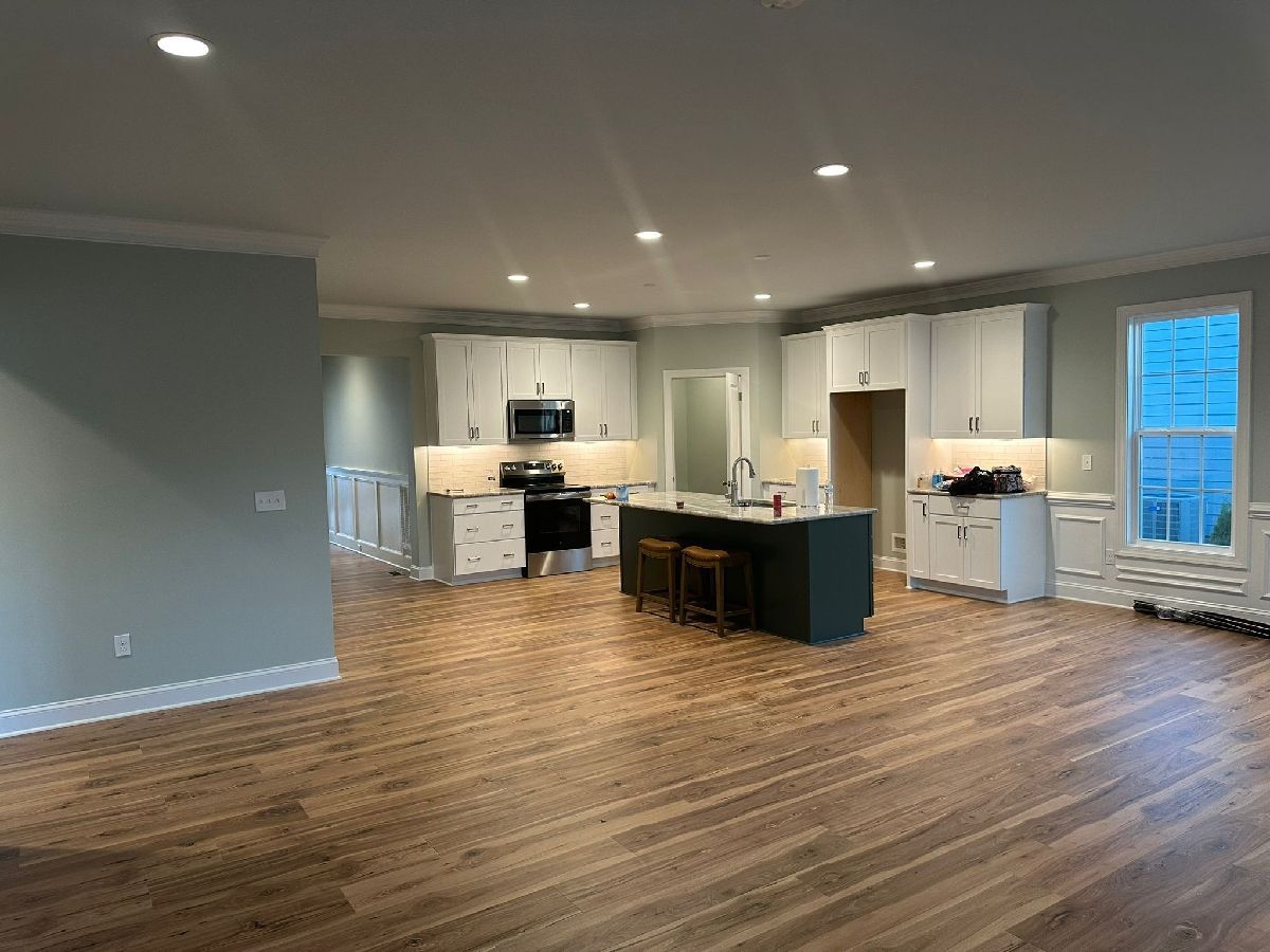 Spacious kitchen with wood floors, white cabinets, and a dark green island. Recessed lighting.