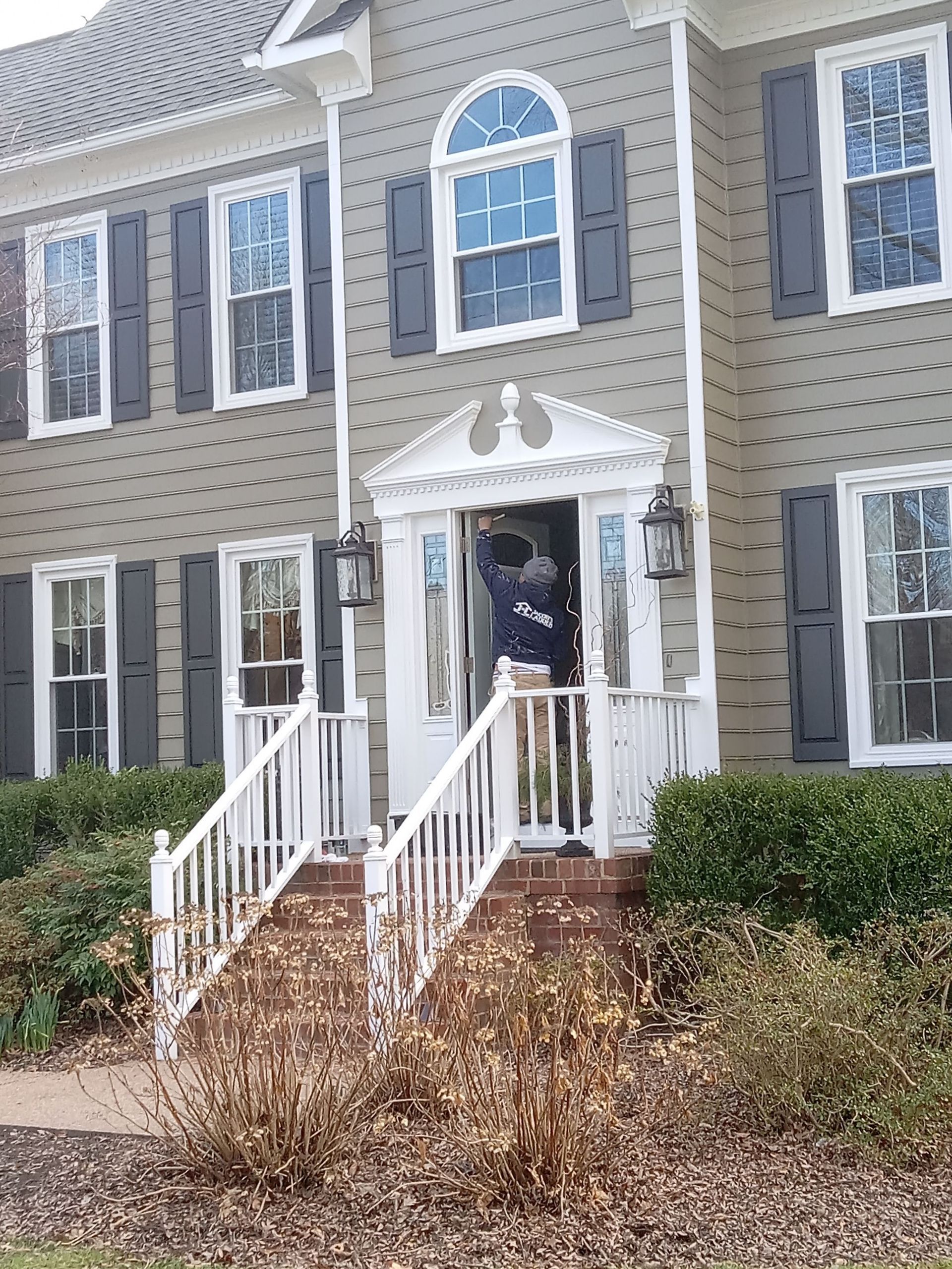 Gray house with white trim, porch, and shutters. Front door open, person visible.