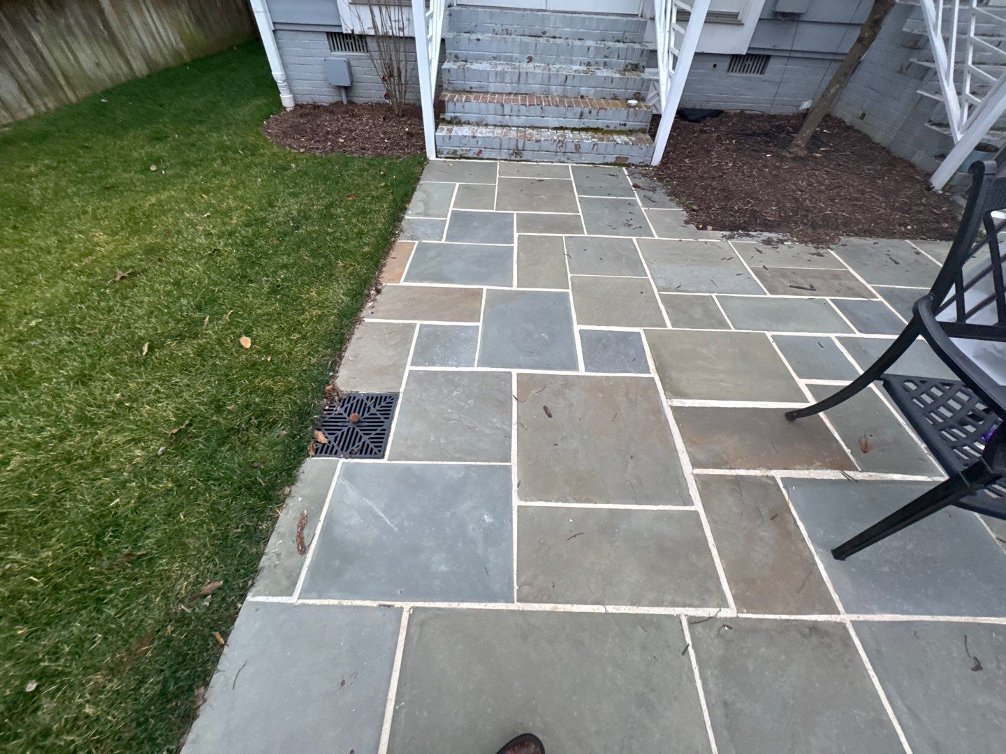 Stone patio with green grass, leading to stairs and a house entrance.