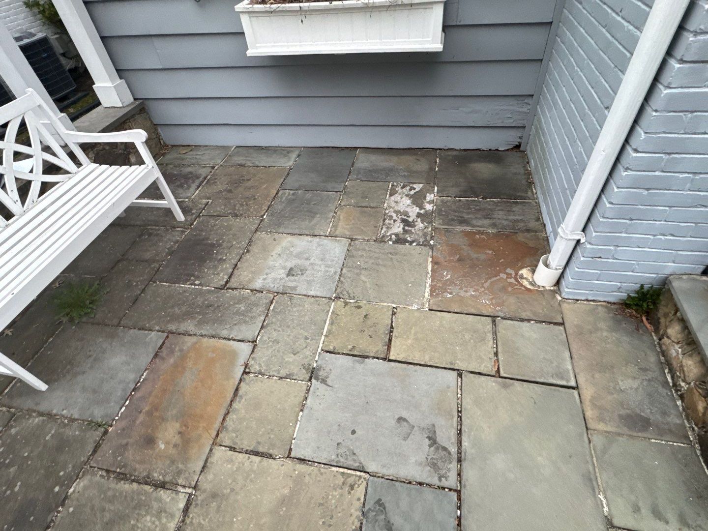 Stone patio with a white bench, and a building with gray siding.