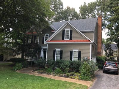 Two-story house with green siding, black shutters, and red trim, surrounded by trees and a car in the driveway.
