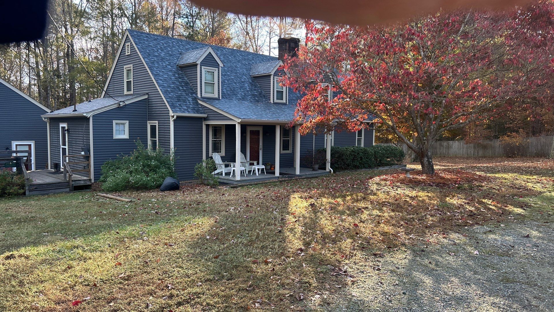 Blue house with dormers, porch, and red-leafed tree in autumn.