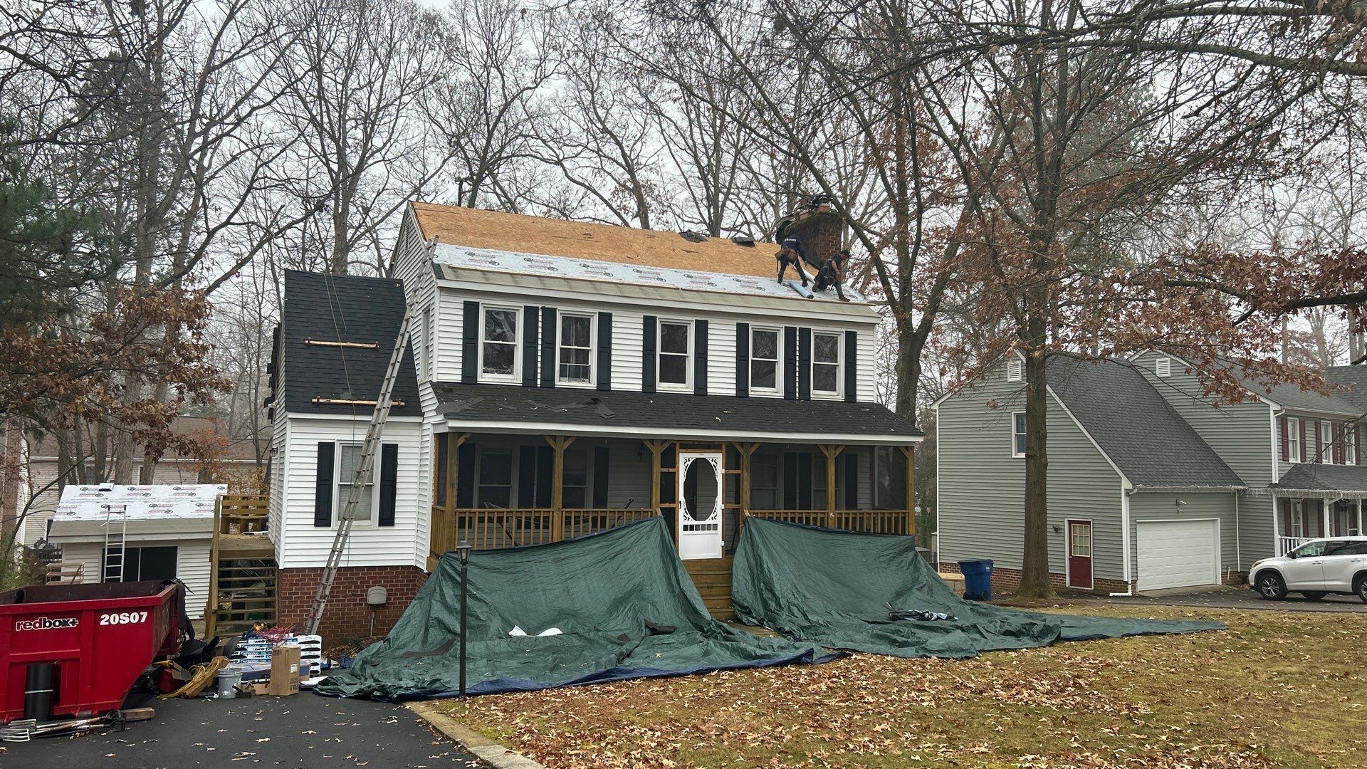 House with roof partially replaced; tarp protects below; worker on roof.
