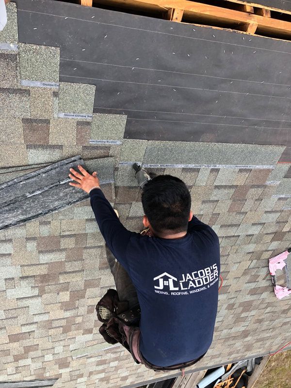 Roofer installing shingles on a roof. The roofer is wearing a blue shirt and working on a roof.