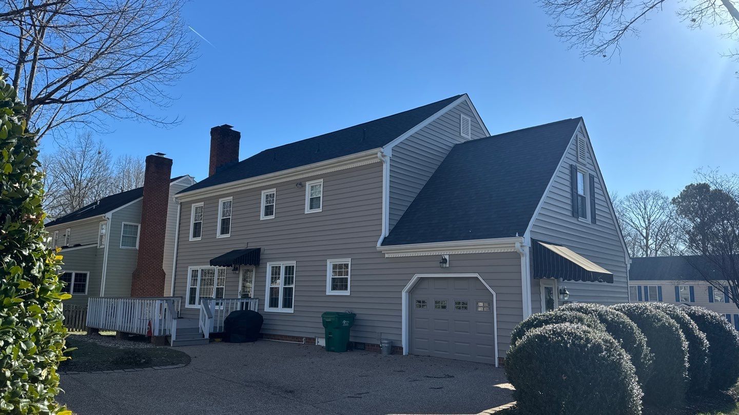 Two-story house with gray siding, black roof, two chimneys, and a garage door under a blue sky.