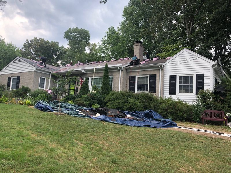Roofers working on a residential roof, with debris tarp in yard, cloudy sky overhead.