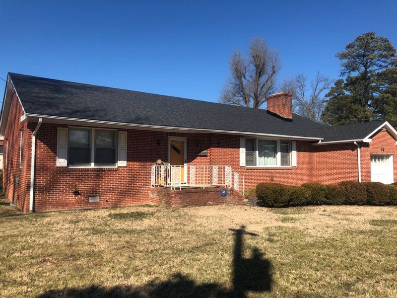 Red brick ranch house with new black roof, white trim, and a small front porch on a sunny day.