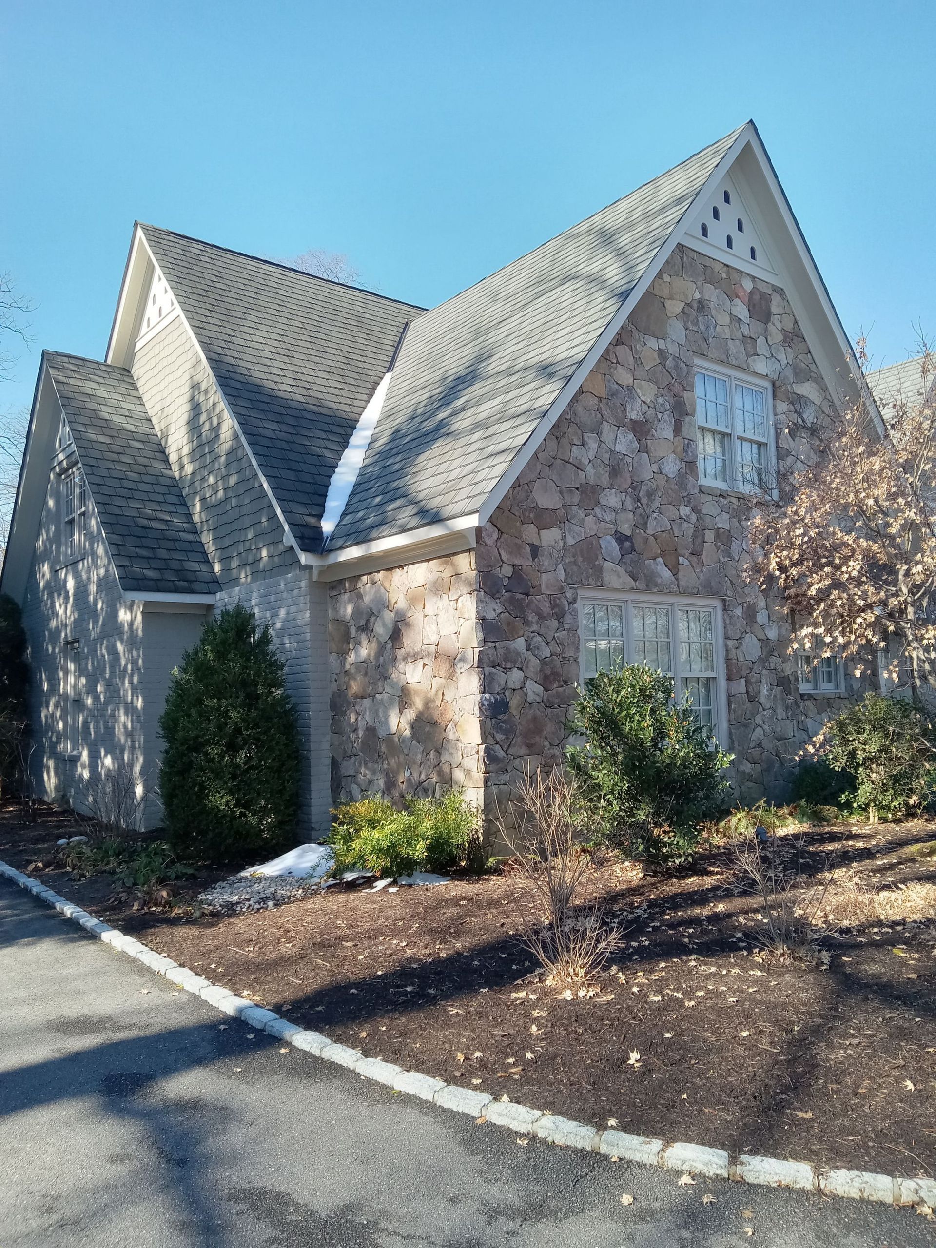 Stone-walled house with a gray roof and windows on a sunny day. A small amount of snow on the ground.