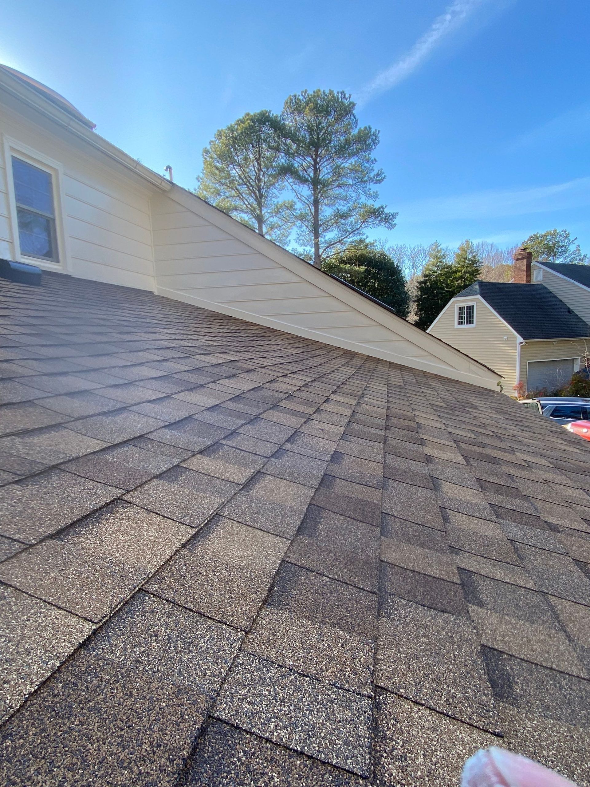 Asphalt shingle roof with a light-colored siding on a sunny day.