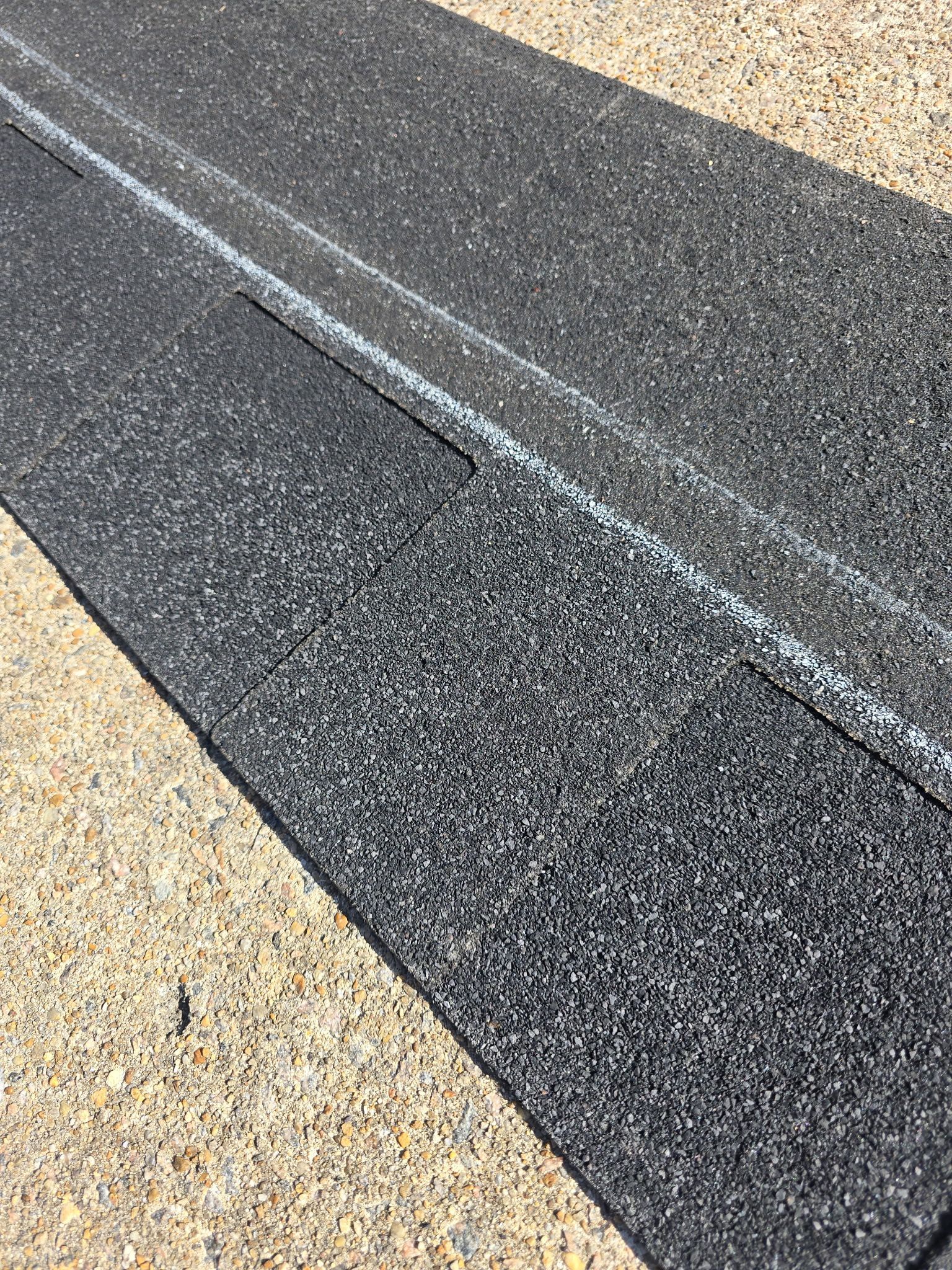 Dark textured roofing material with white lines, likely for guiding installation, on a tan surface.