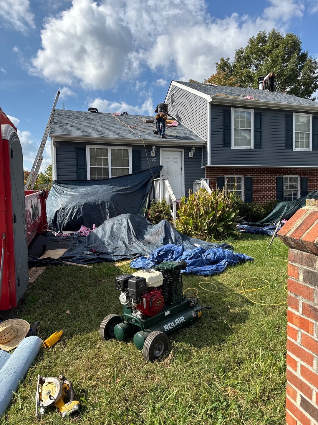 Roofers working on a house with dark blue siding, using equipment on the lawn.