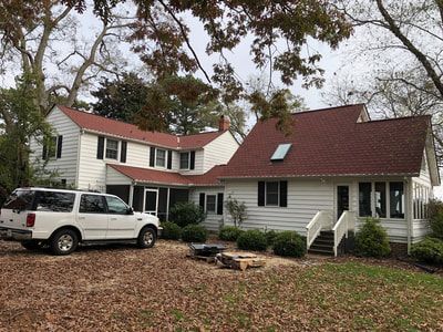 White house with red roof, white SUV parked in front. Leaves on the ground, overcast sky.