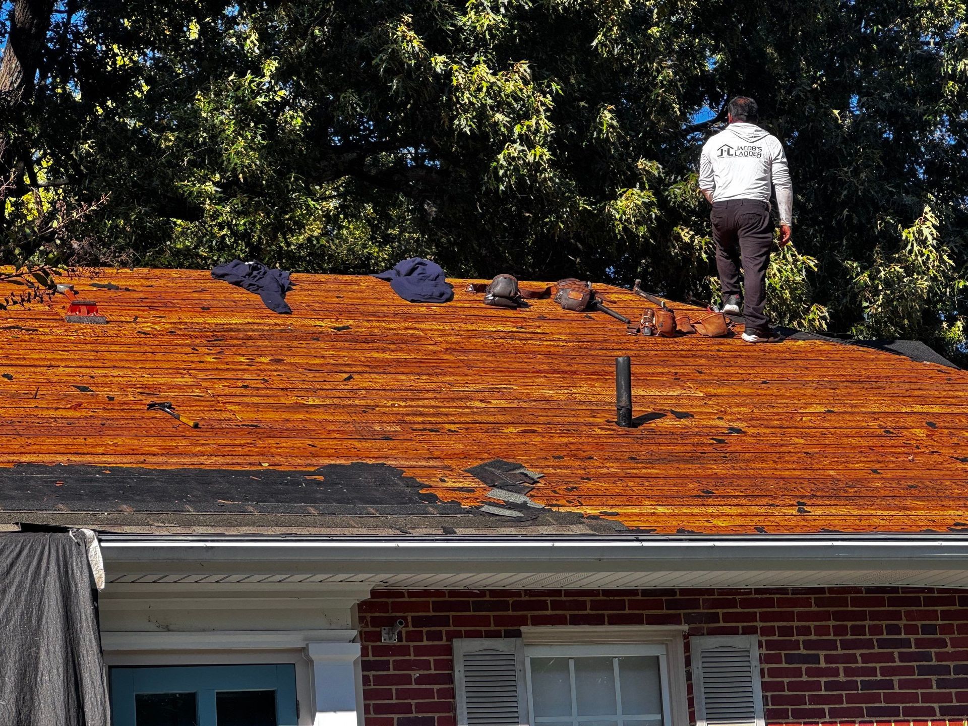 Person walking on a damaged roof. Red brick house with brown, exposed wood roof.