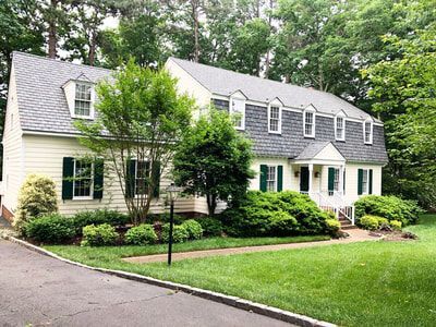 Two-story house with yellow siding, gray roof, green shutters, and well-kept landscaping.