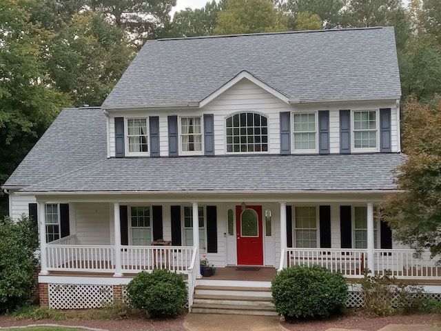 Two-story white house with a red door, gray roof, and black shutters, porch with white railings.